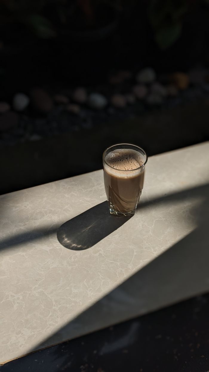 A subtle and serene image of a glass of coffee catching sunlight on a marble table.