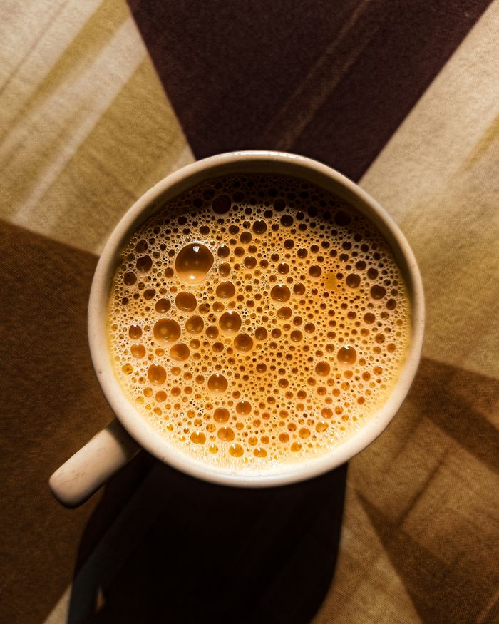 Close-up of frothy milk tea in a cup on a geometric patterned tablecloth.