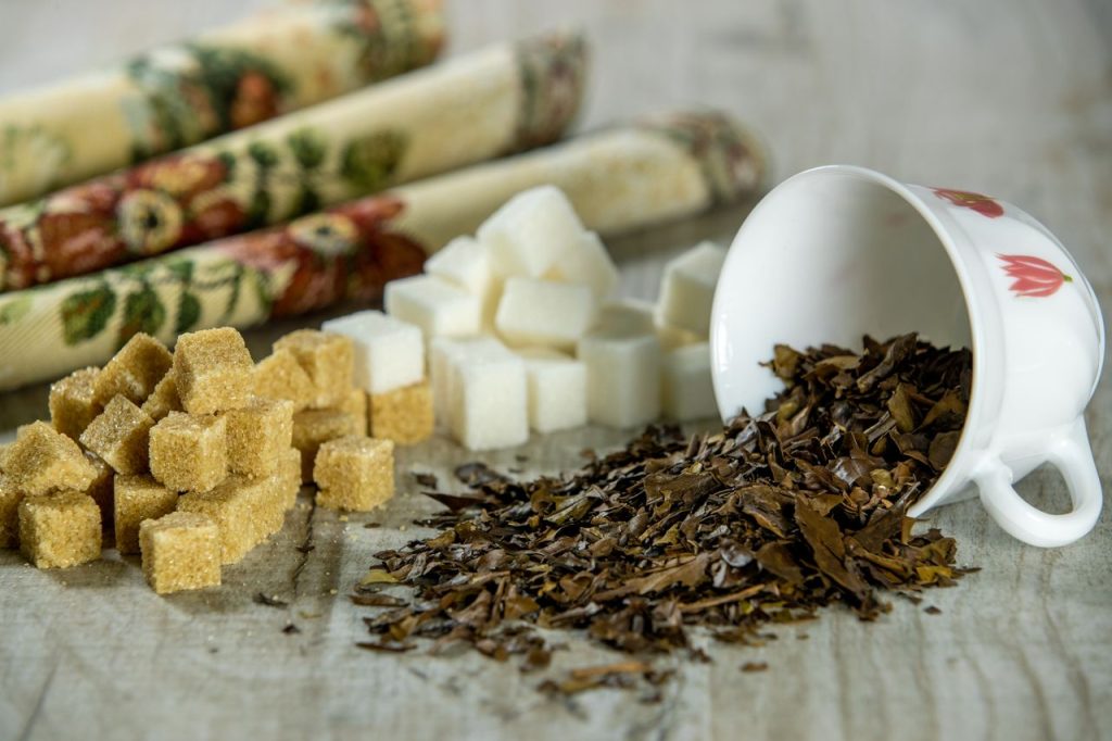 Artistic display of loose tea leaves and sugar cubes with a floral cloth background.